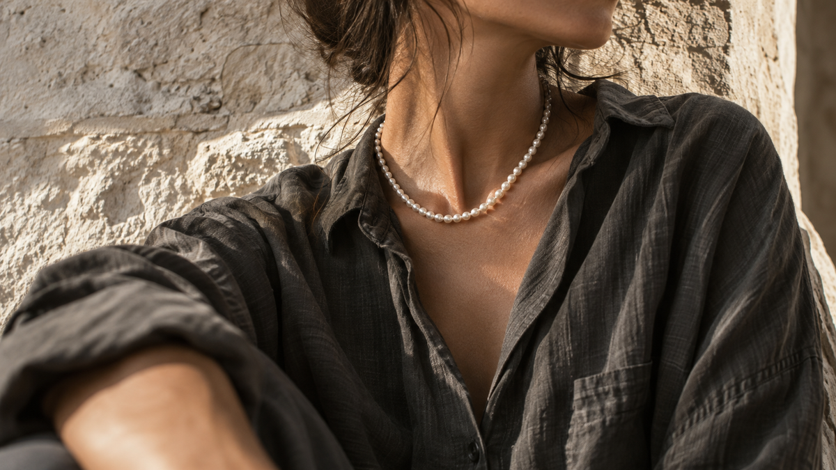 Unisex pearl necklace styled with an oversized charcoal linen shirt against sunlit Mediterranean limestone.