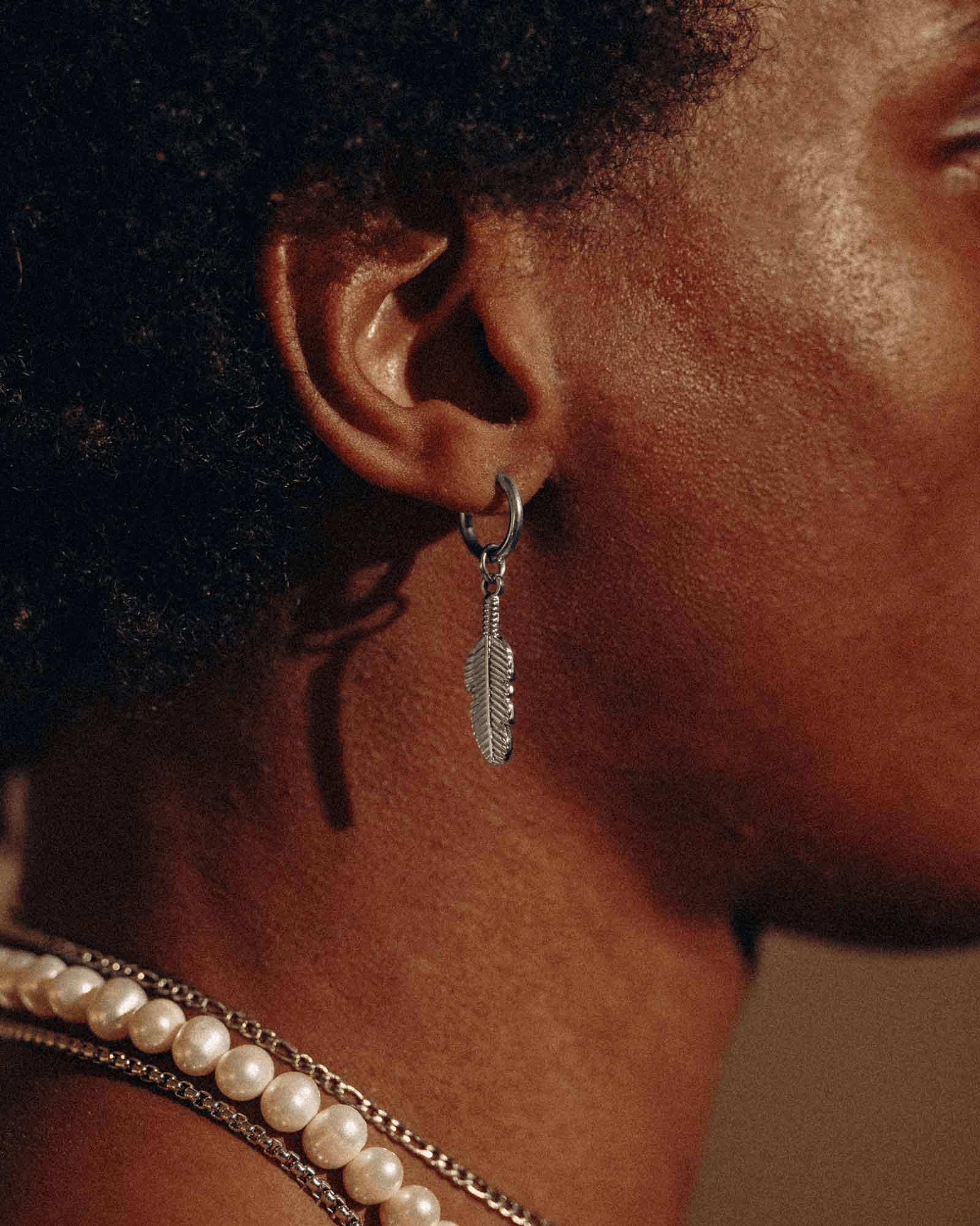 Earrings for Men featuring a silver feather design worn on the ear with a close-up of a person's profile.