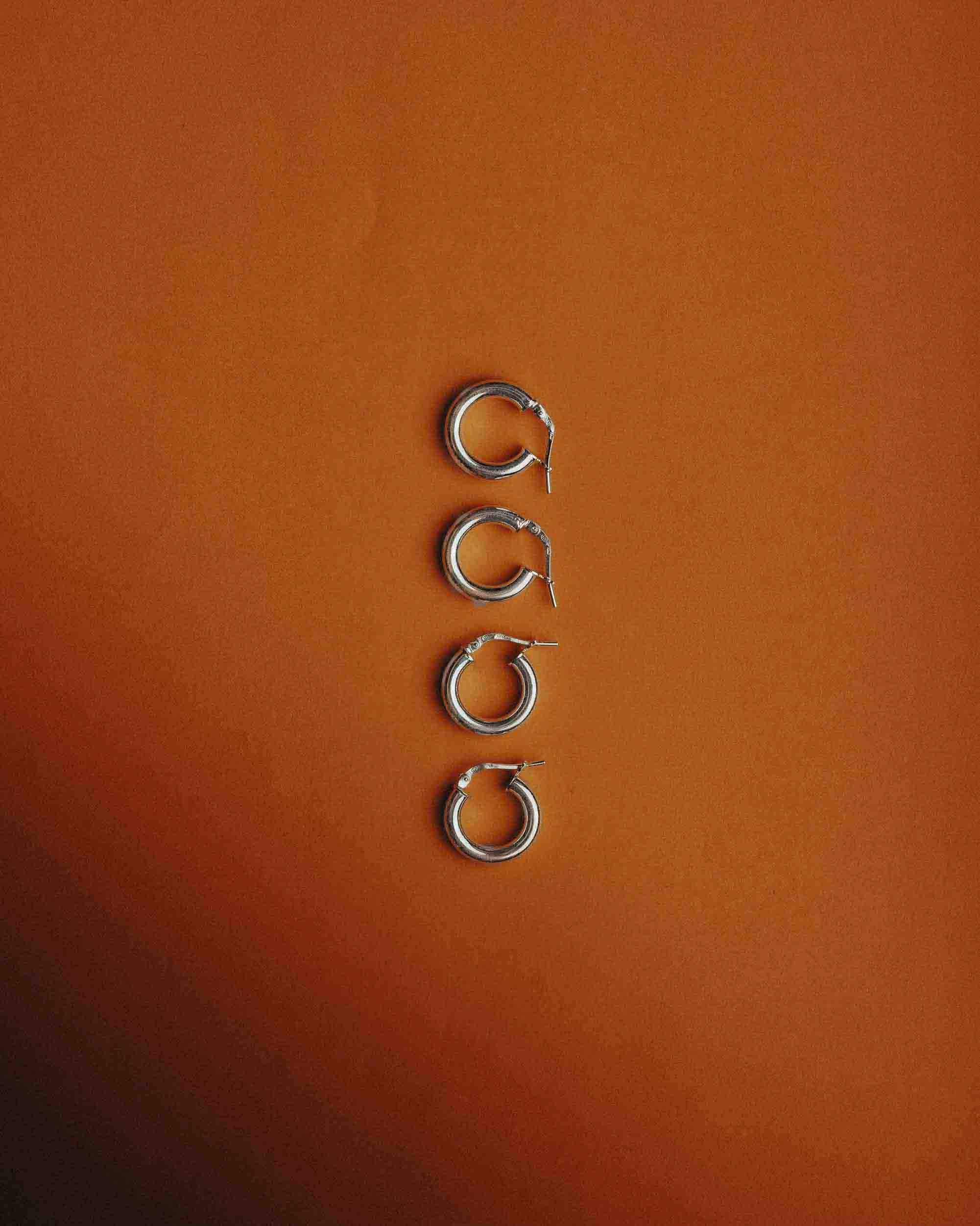 Four pairs of 925 silver earrings for men displayed on a warm orange background, showcasing modern styles.