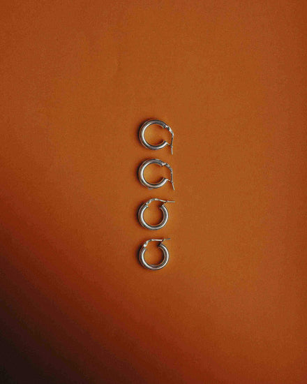 Four pairs of 925 silver earrings for men displayed on a warm orange background, showcasing modern styles.