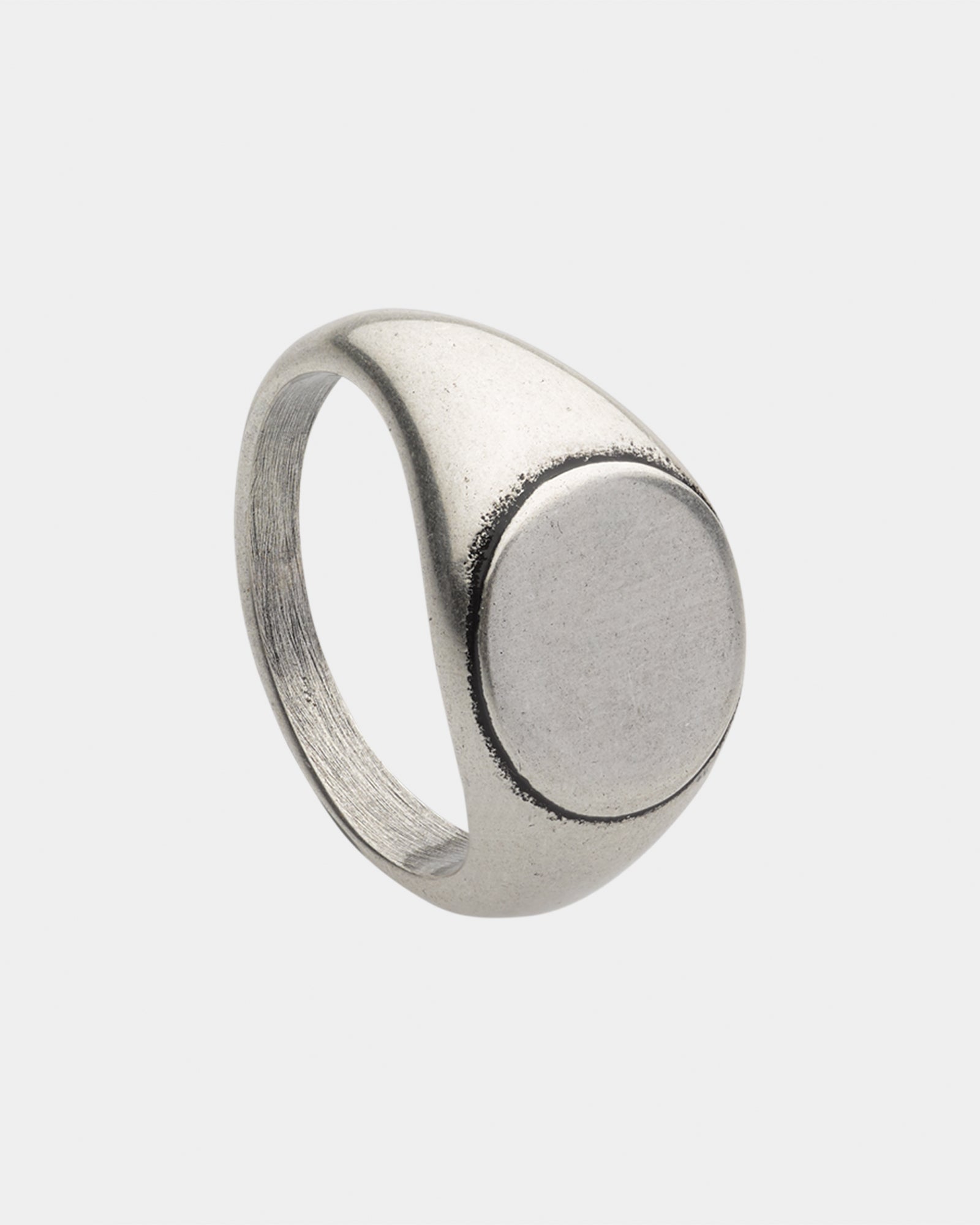 A silver-colored signet ring with a smooth, satin finish and a polished top, displayed against a white background.