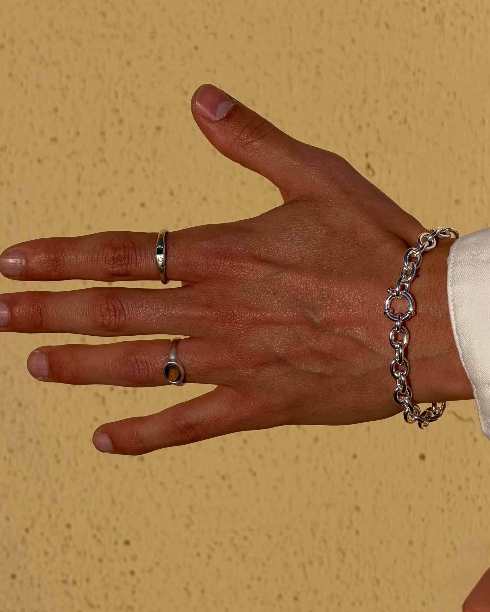Hand wearing two rings and a bracelet against a beige background