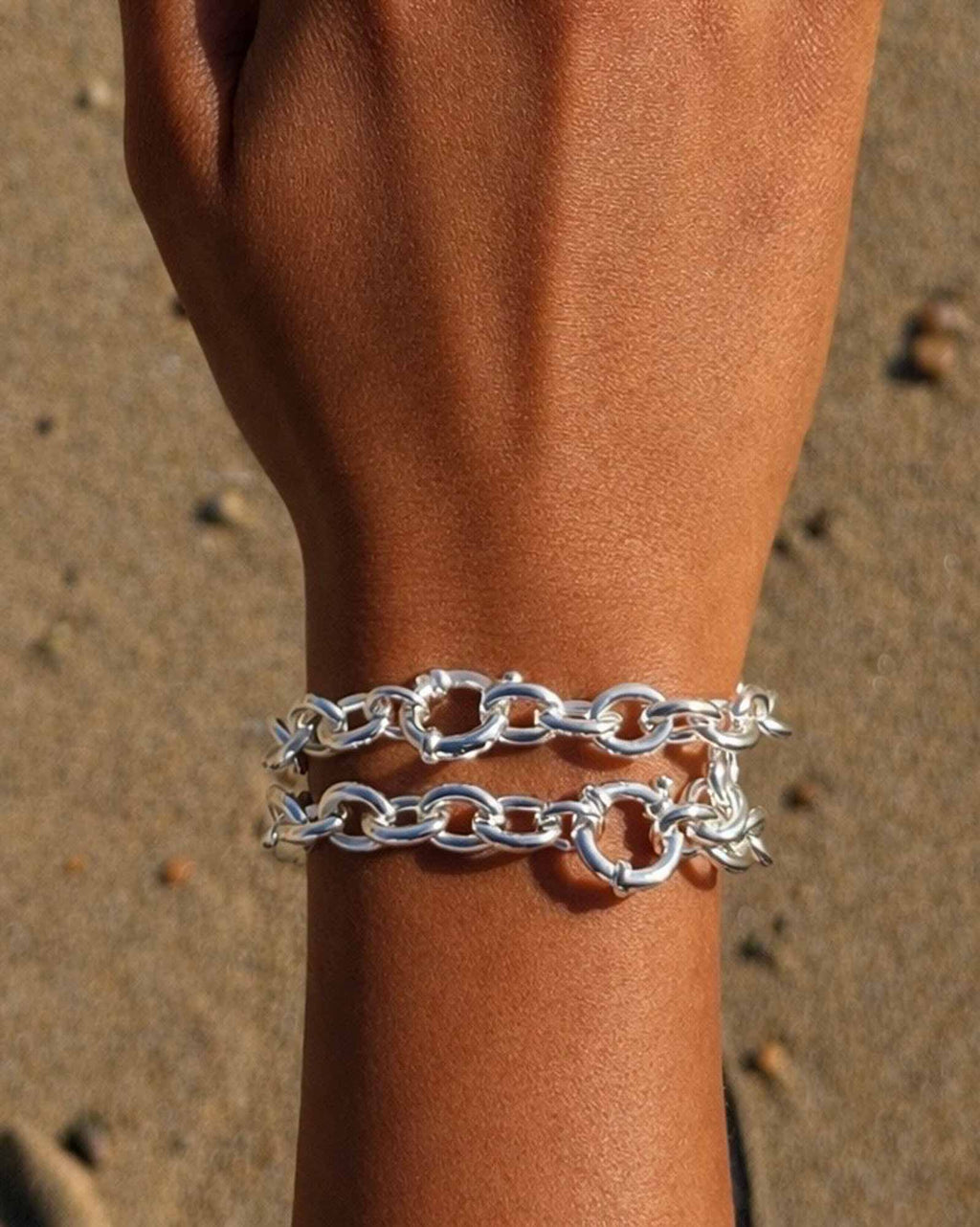 Silver chain bracelet on a wrist with a sandy background