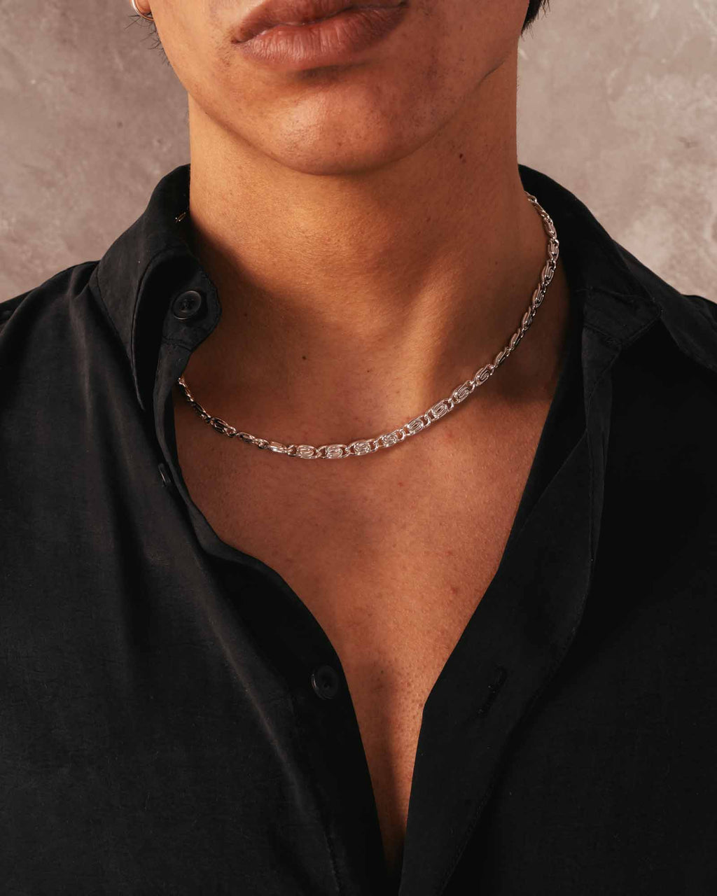 Person wearing a black shirt with a silver chain necklace against a neutral background