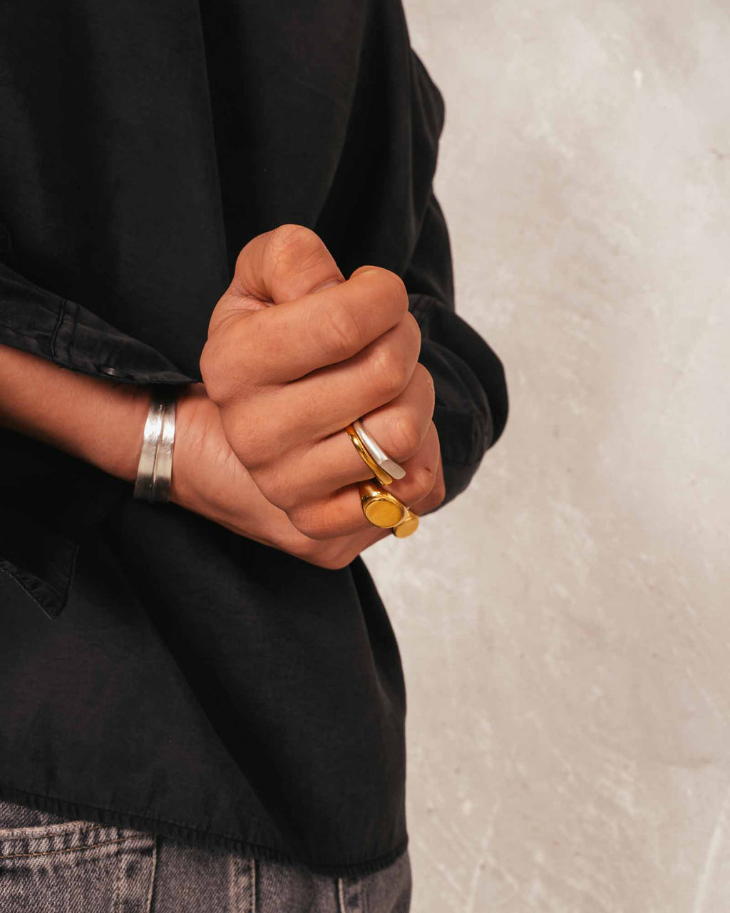 Close-up of a person's hands with gold ring and silver bracelet on a neutral background