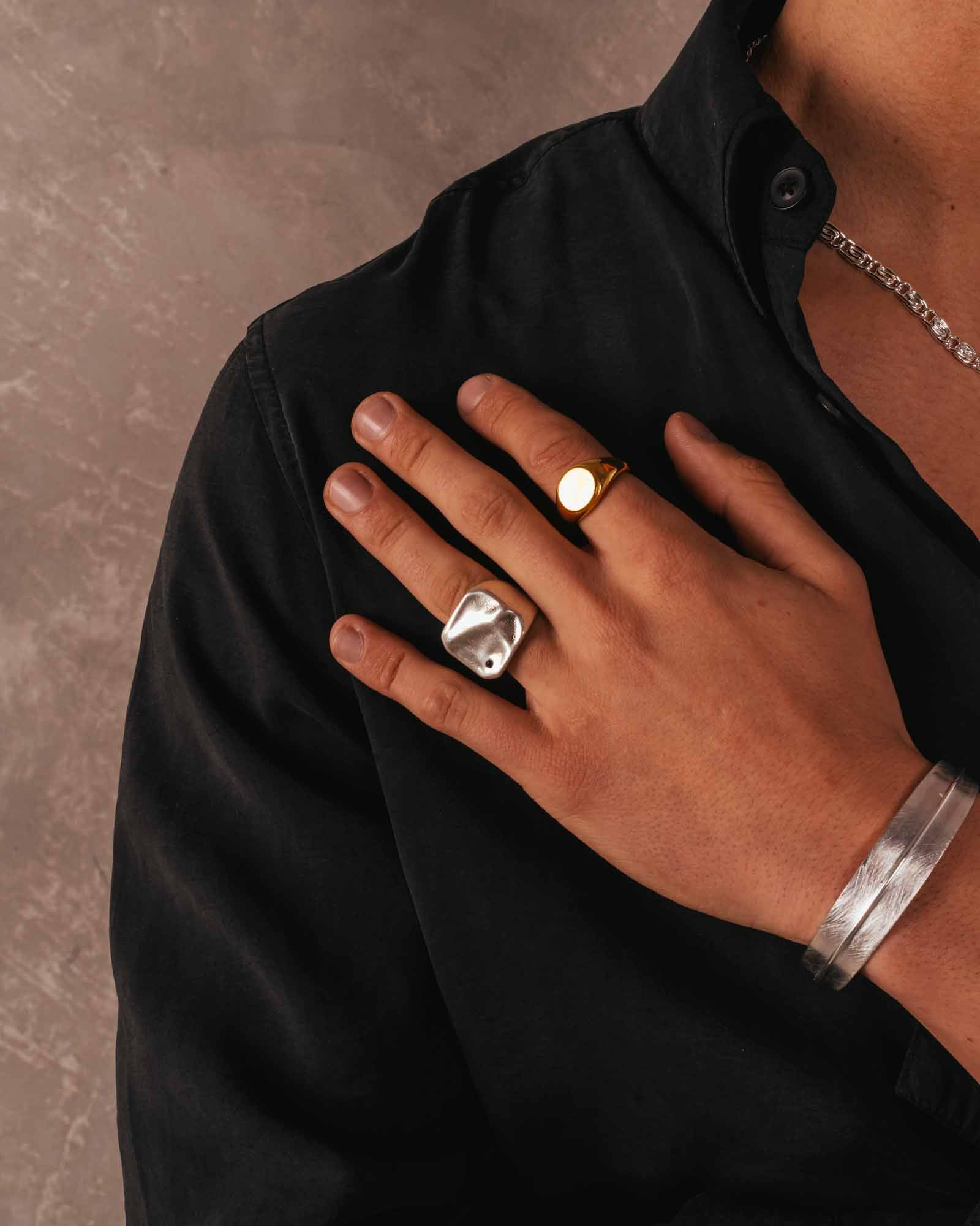 Hand wearing two rings on a black shirt against a brown background