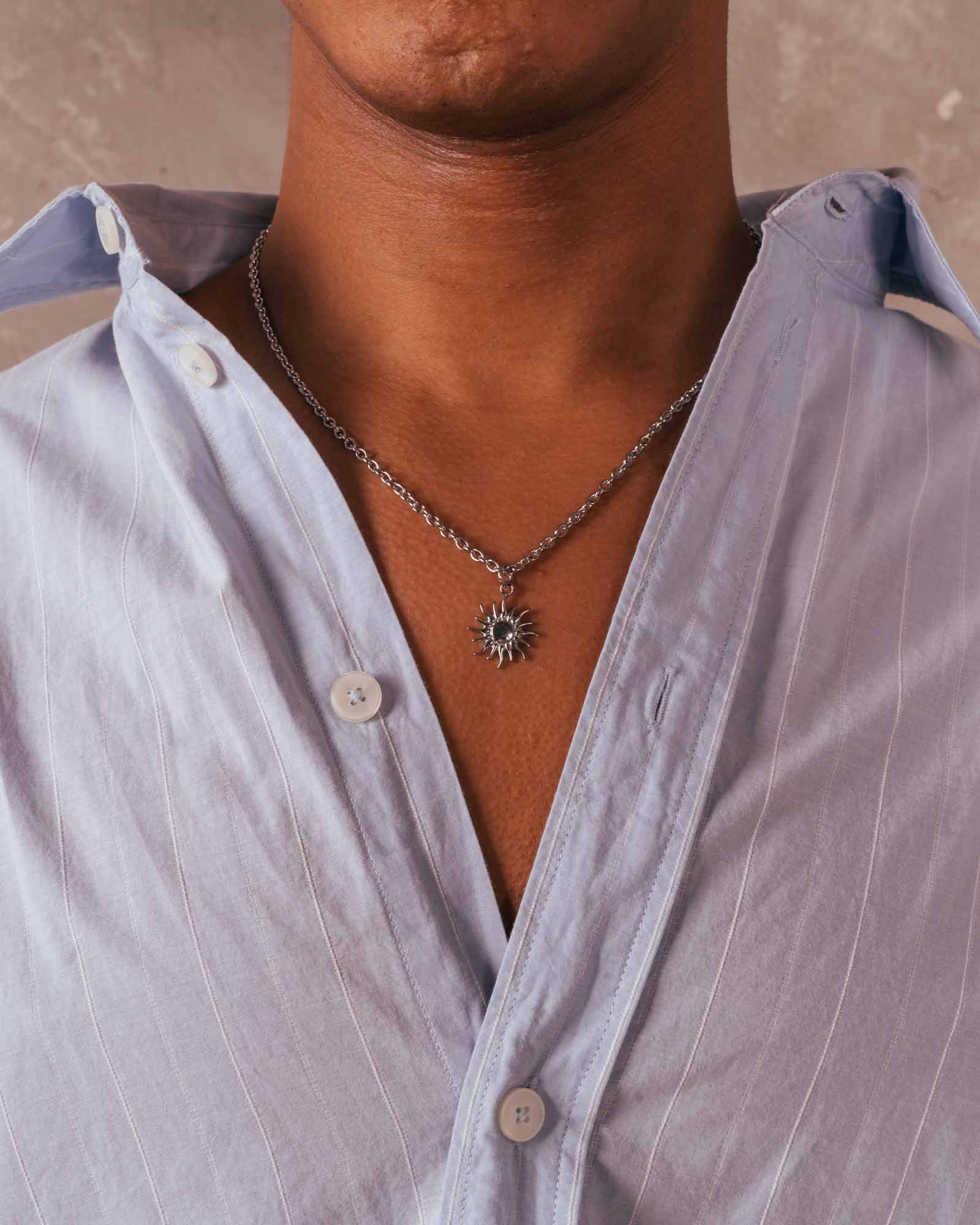 Person wearing a light blue shirt with a necklace featuring a sun pendant.