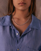 Persona con camisa azul y collar plateado sobre un fondo neutro
