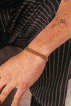Bracciale a catena d’oro su un polso tatuato, su uno sfondo sfocato.