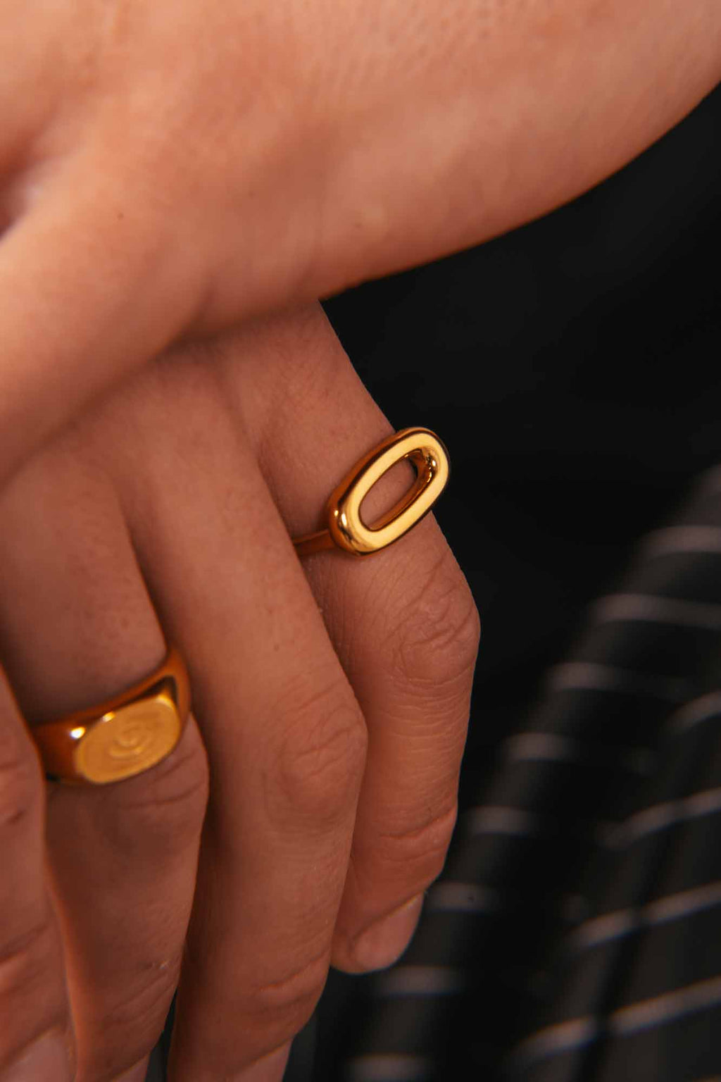 Close-up of a hand wearing two gold rings with a blurred background