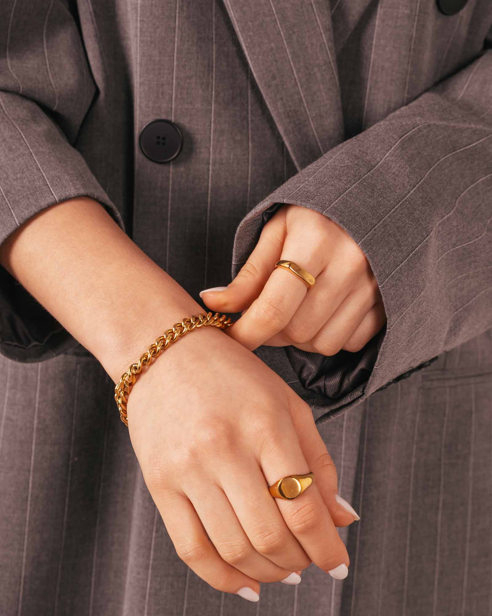 Close-up of hands wearing gold bracelets and rings against a gray pinstripe suit background