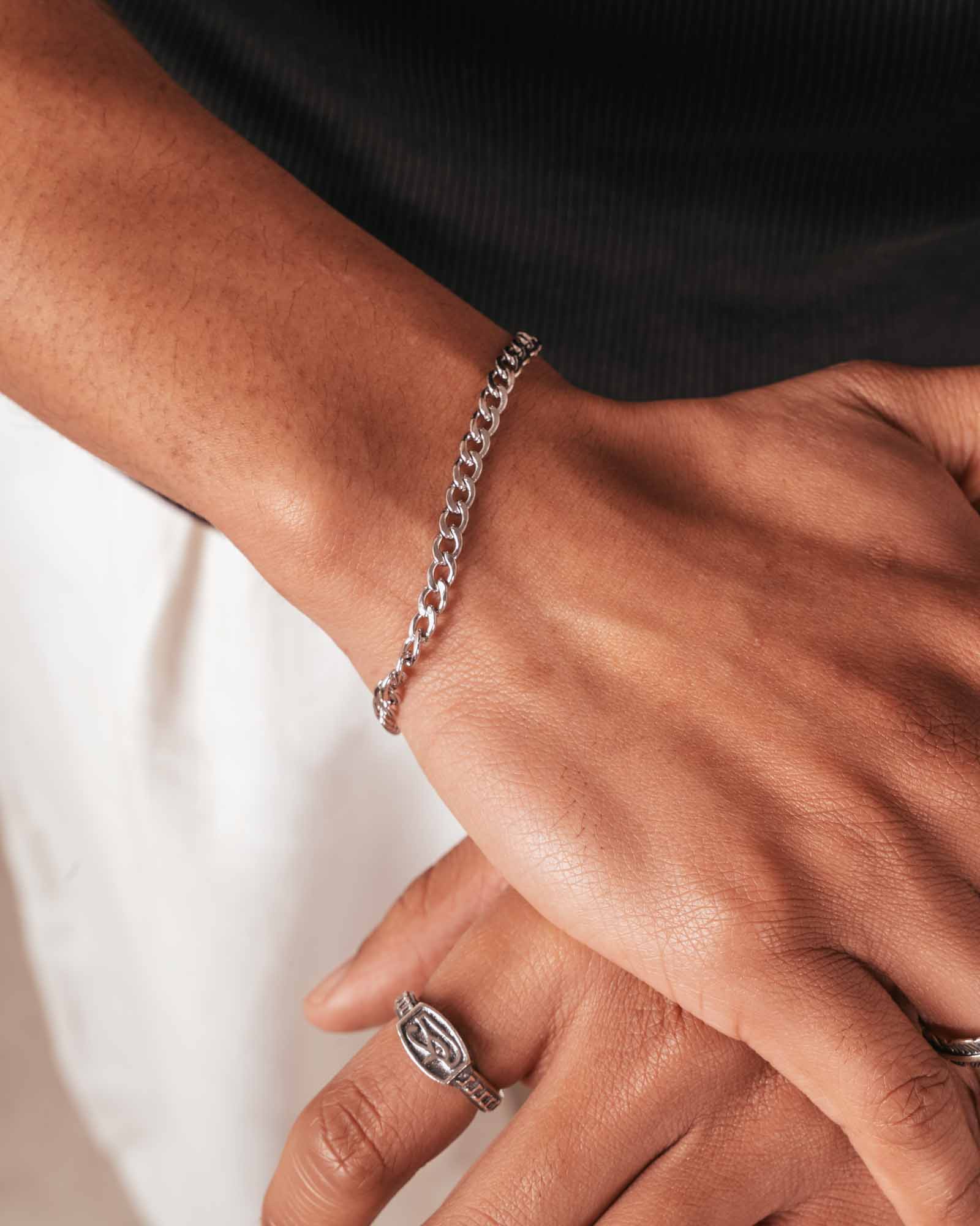 Close-up of a wrist wearing a silver chain bracelet with a ring on a neutral background