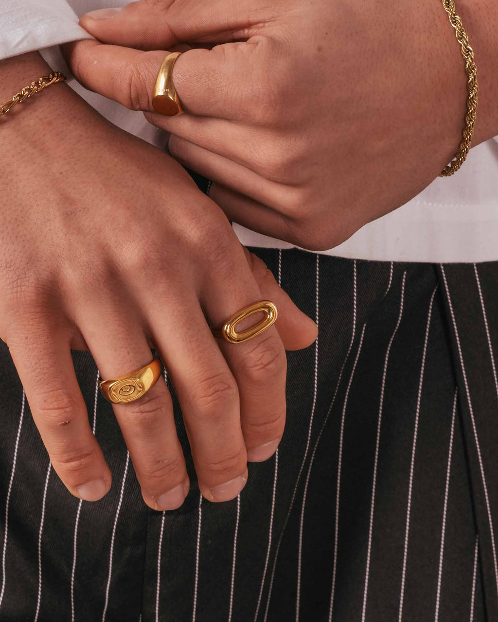 Close-up of hands wearing gold rings with a black pinstripe background