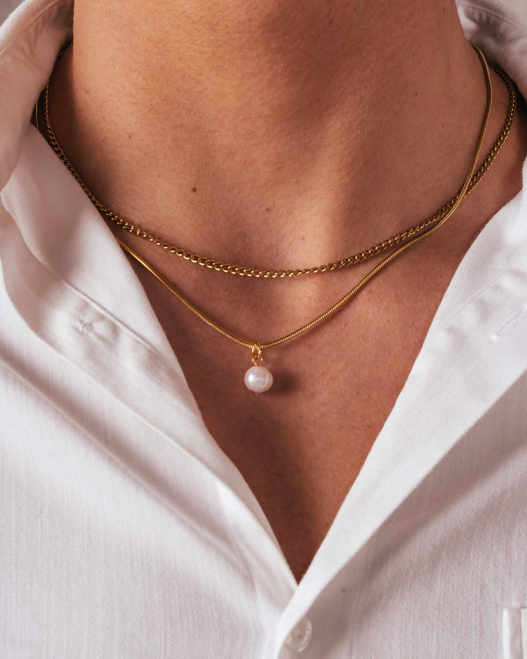 Gold necklace with a pearl pendant worn by a person in a white shirt.