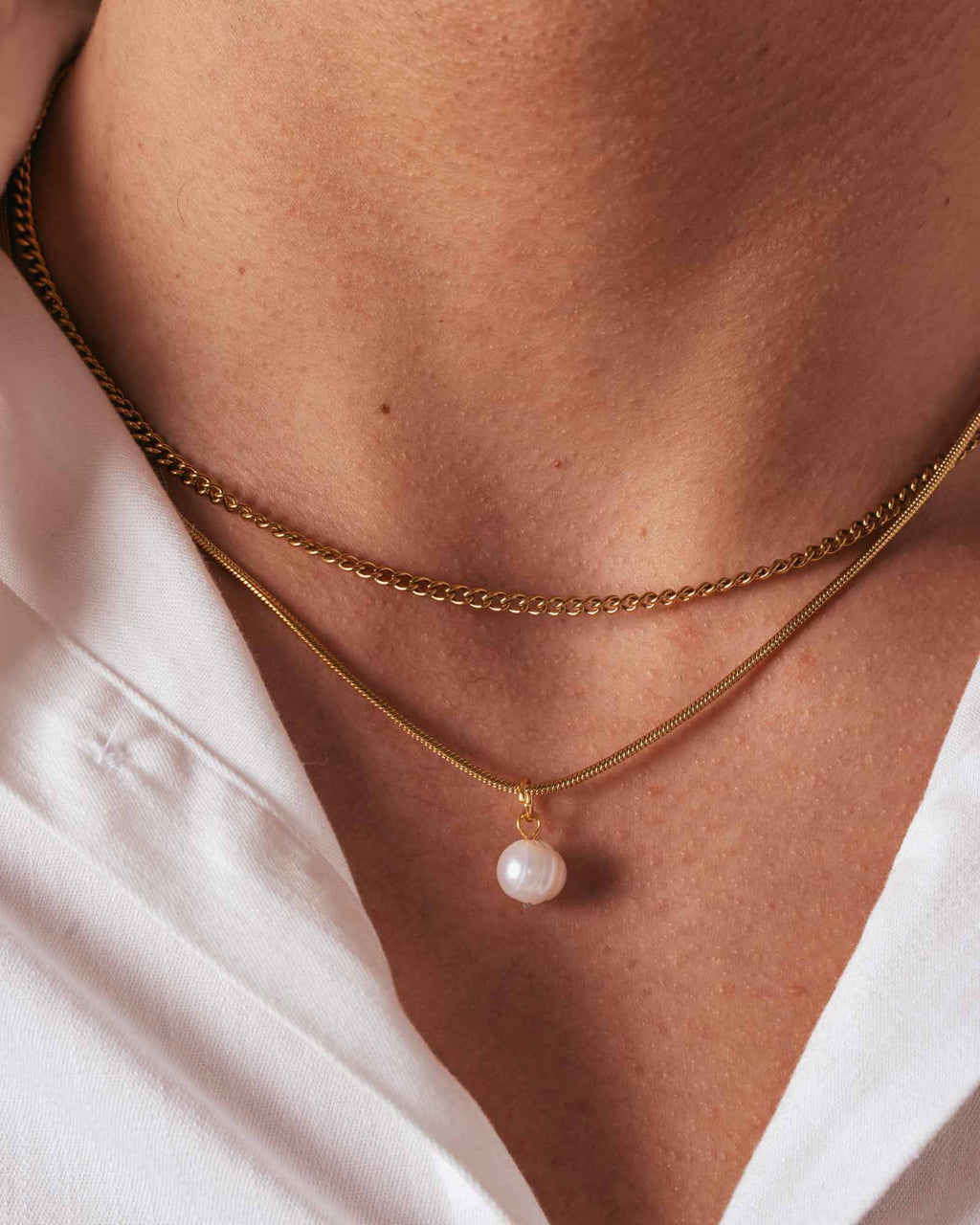 Gold chain necklace with a pearl pendant on a person wearing a white shirt.