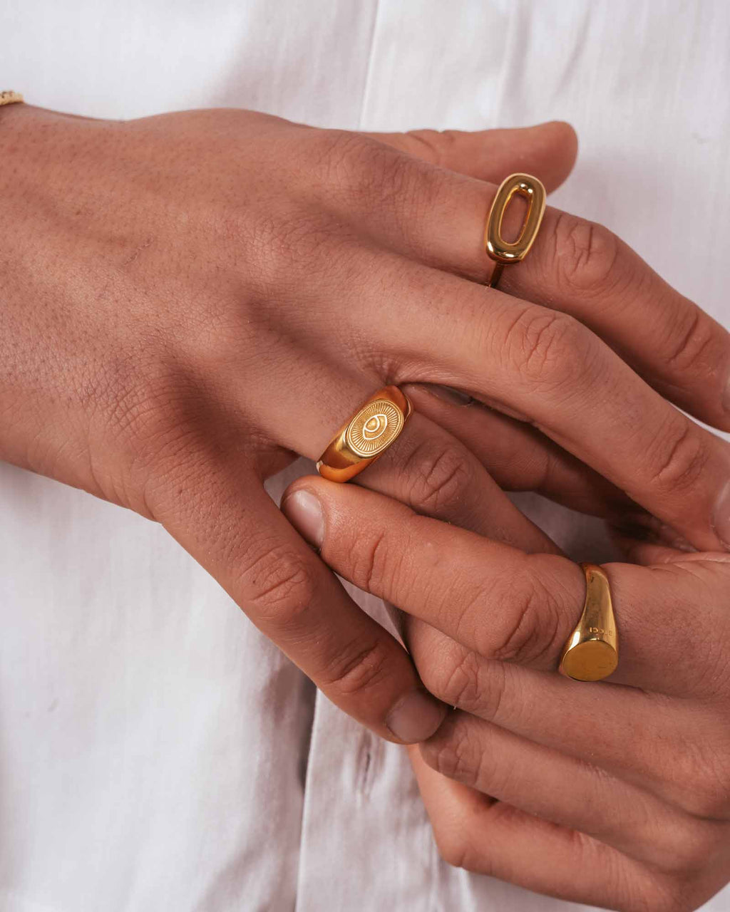 Close-up of hands wearing golden sunray rings on a white background
