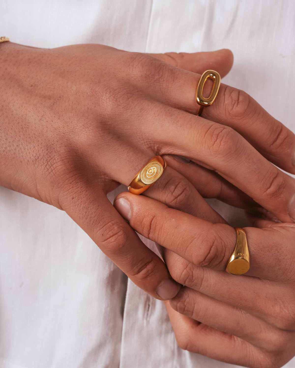 Close-up of hands wearing golden sunray rings on a white background