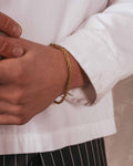 Gold bracelet on a wrist with a white shirt and black pants in the background