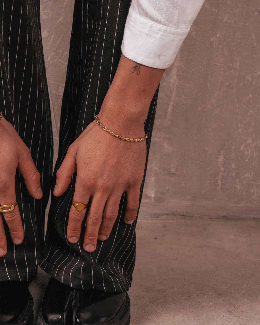 Person wearing a gold bracelet and ring on a neutral background