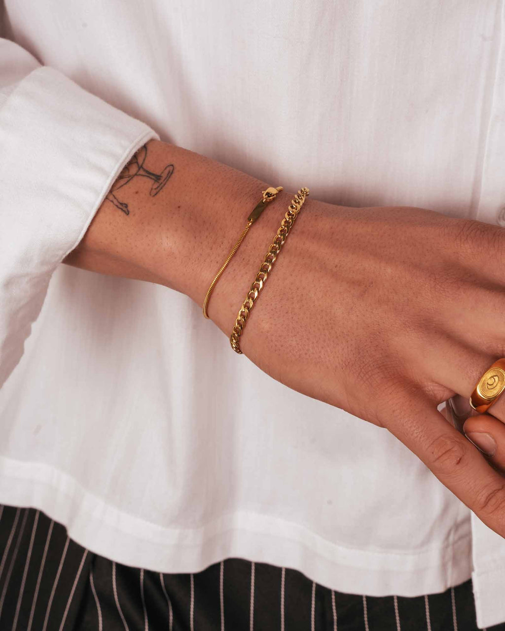 Close-up of a wrist wearing gold bracelets with a white shirt background