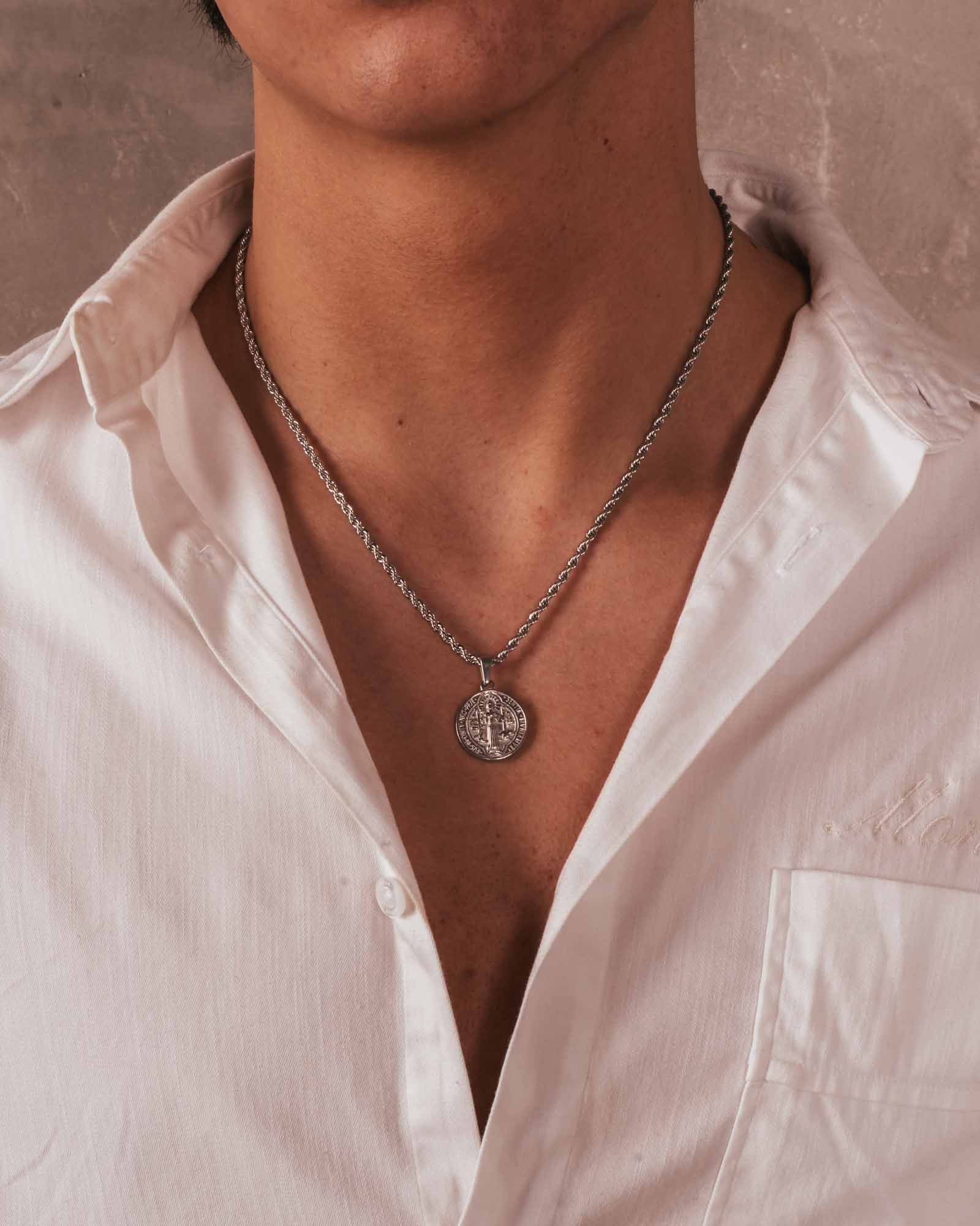 Person wearing a white shirt with a necklace featuring a circular pendant.