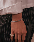 Primo piano di una mano con un bracciale a catena rolo color argento su sfondo neutro