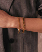 Person wearing a gold Cuban chain bracelet on a neutral background