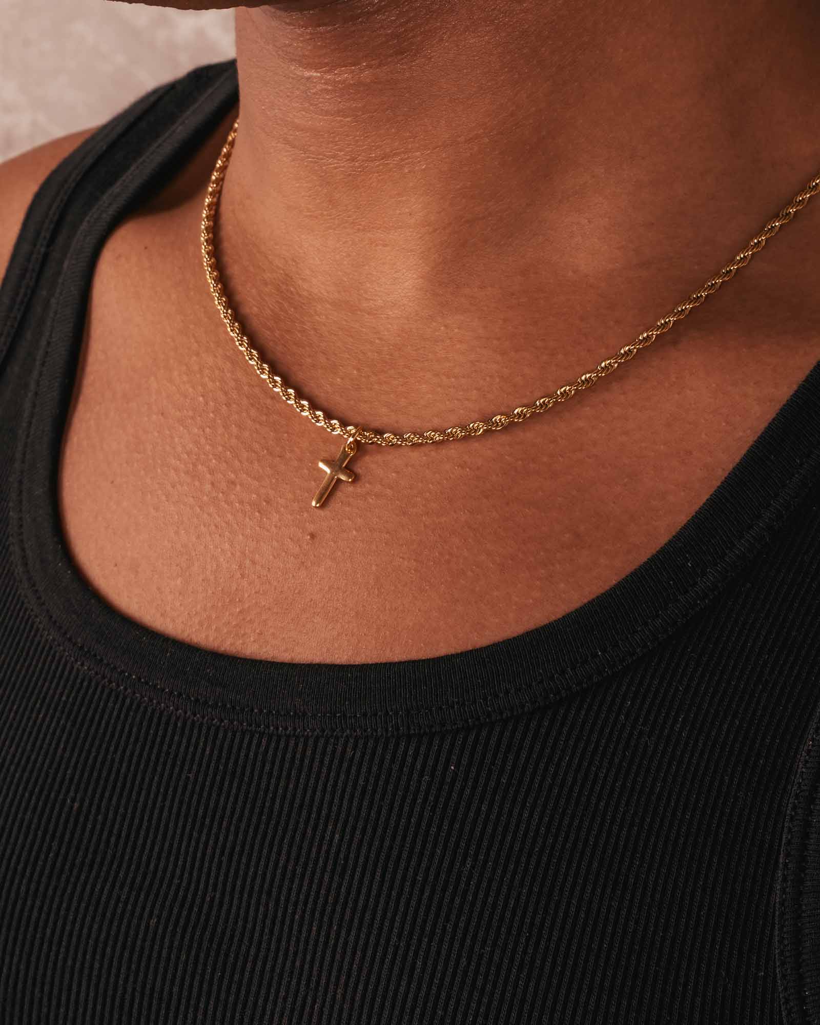 Gold necklace with a cross pendant on a person wearing a black top.