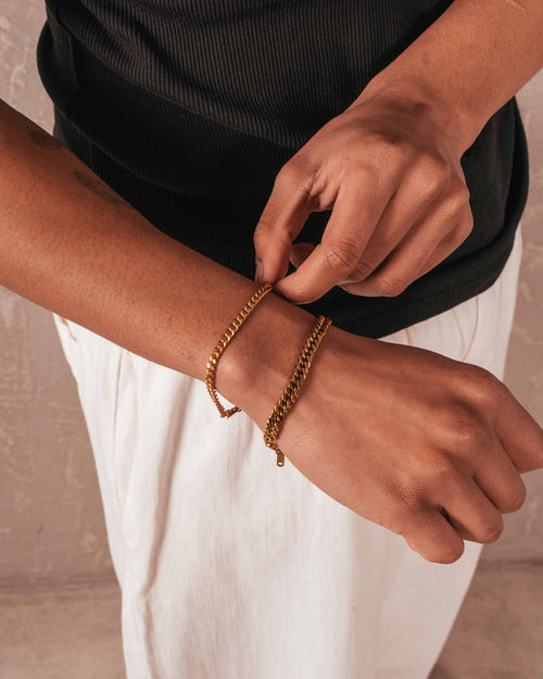 Person wearing gold bracelets on a neutral background