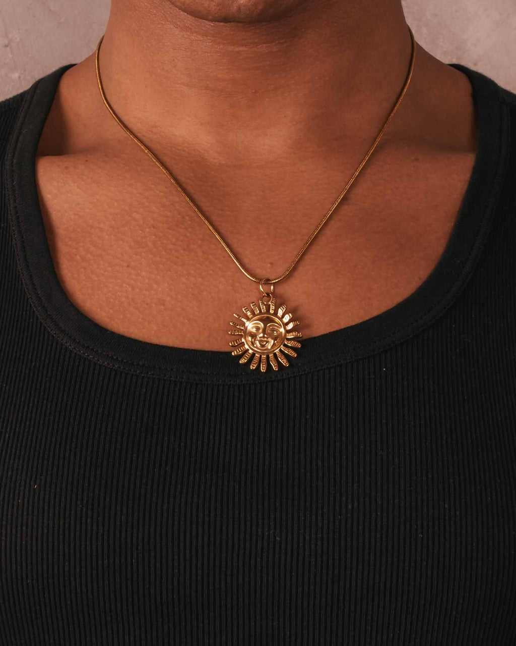 Gold sun-shaped pendant necklace on a person wearing a black top.