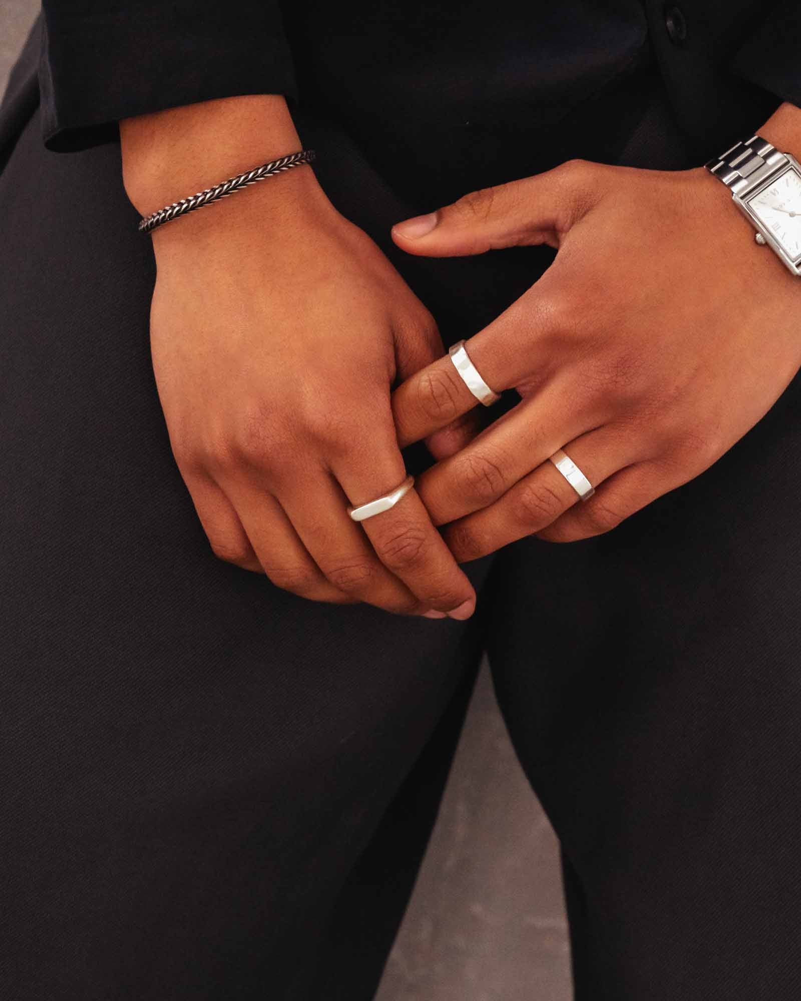 Close-up of two hands with silver rings on a black background