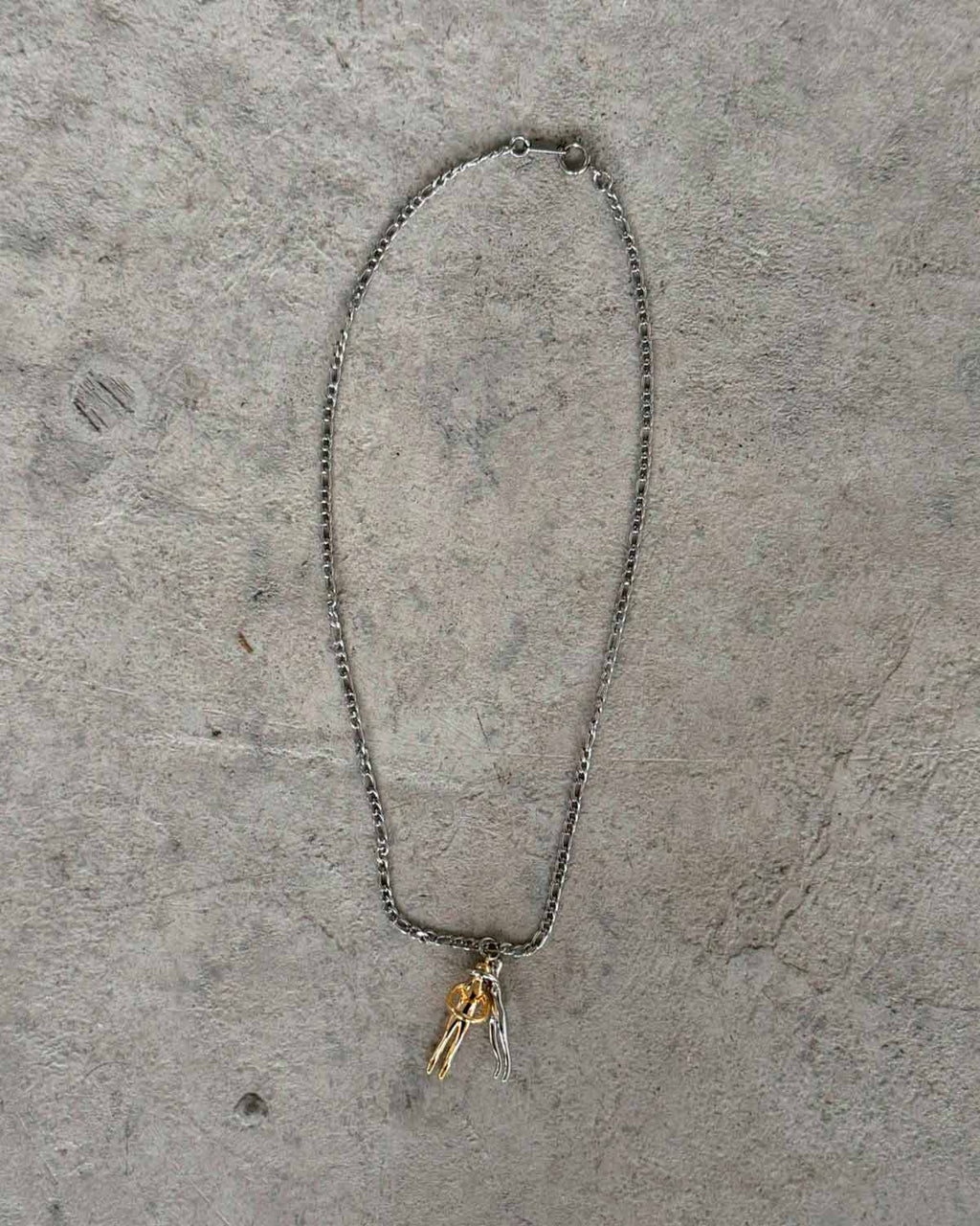 Couple Hug Necklace featuring intertwining figures in silver and gold on a minimalist chain background.