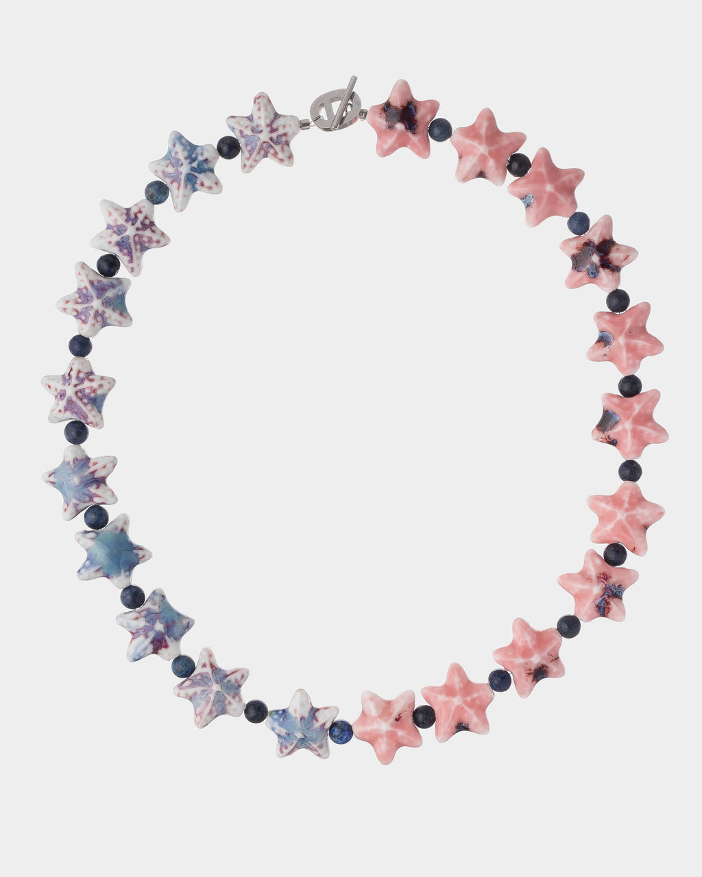 A beaded necklace featuring alternating star-shaped beads in pink, blue, and white, separated by small dark round beads, on a light gray background.