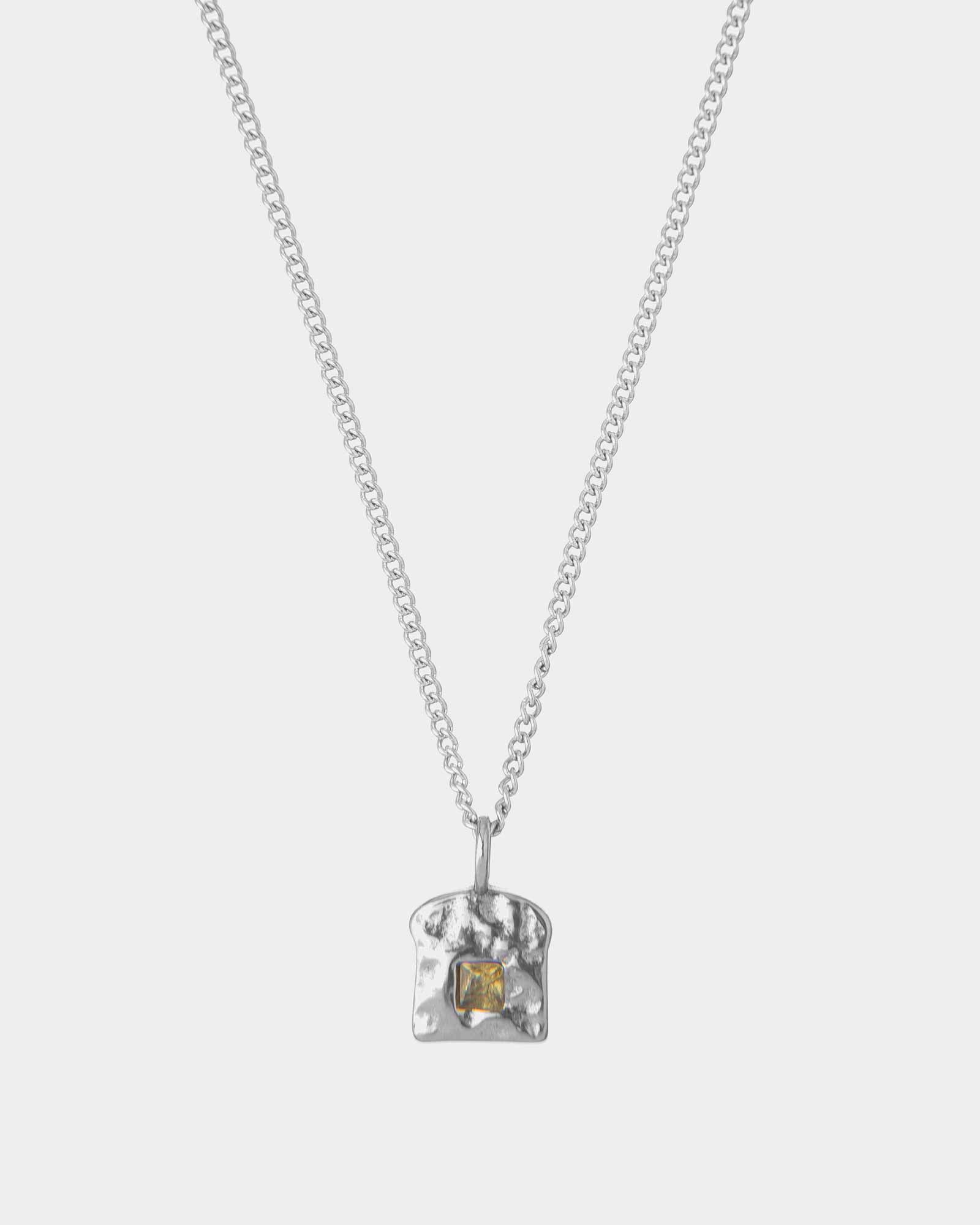 Silver necklace with a textured pendant and a emerald on a white background