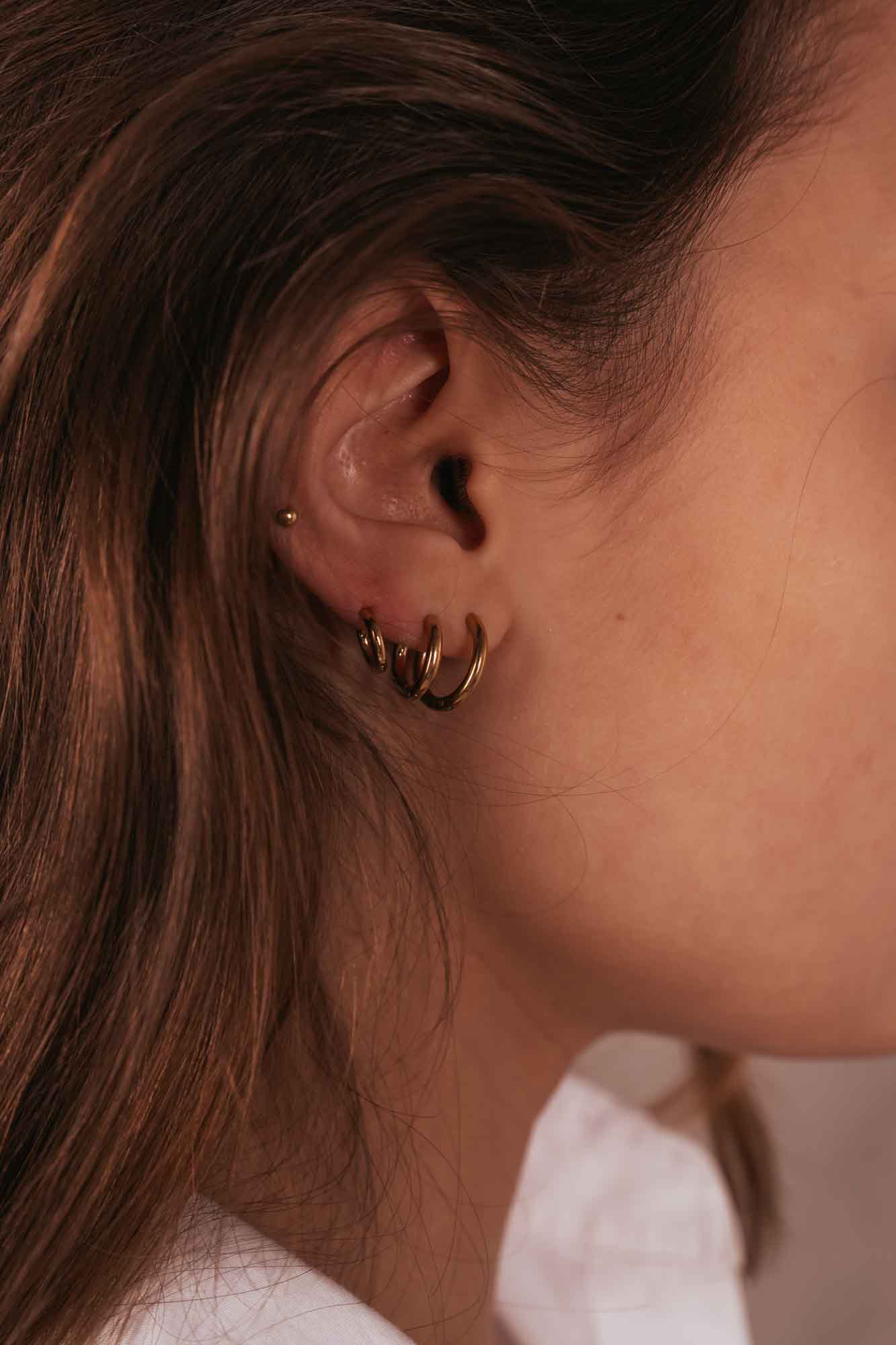 Close-up of an ear wearing a gold hoop earring with a blurred background