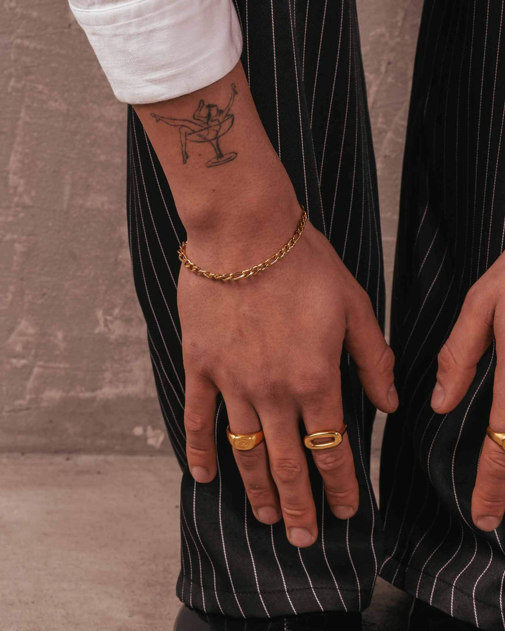 Hand with gold jewelry wearing a black pinstripe suit.