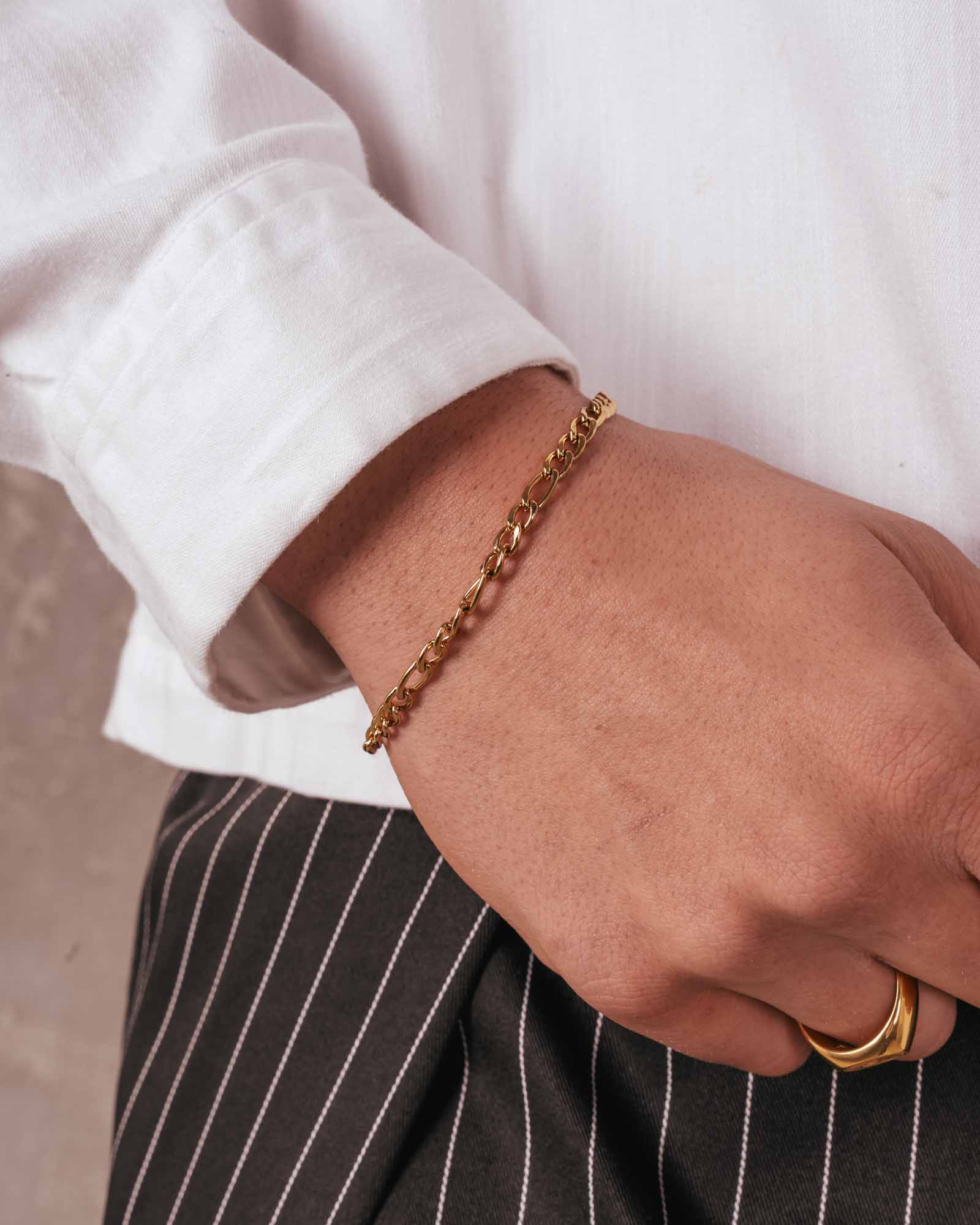 Hand wearing a gold bracelet and ring on a neutral background