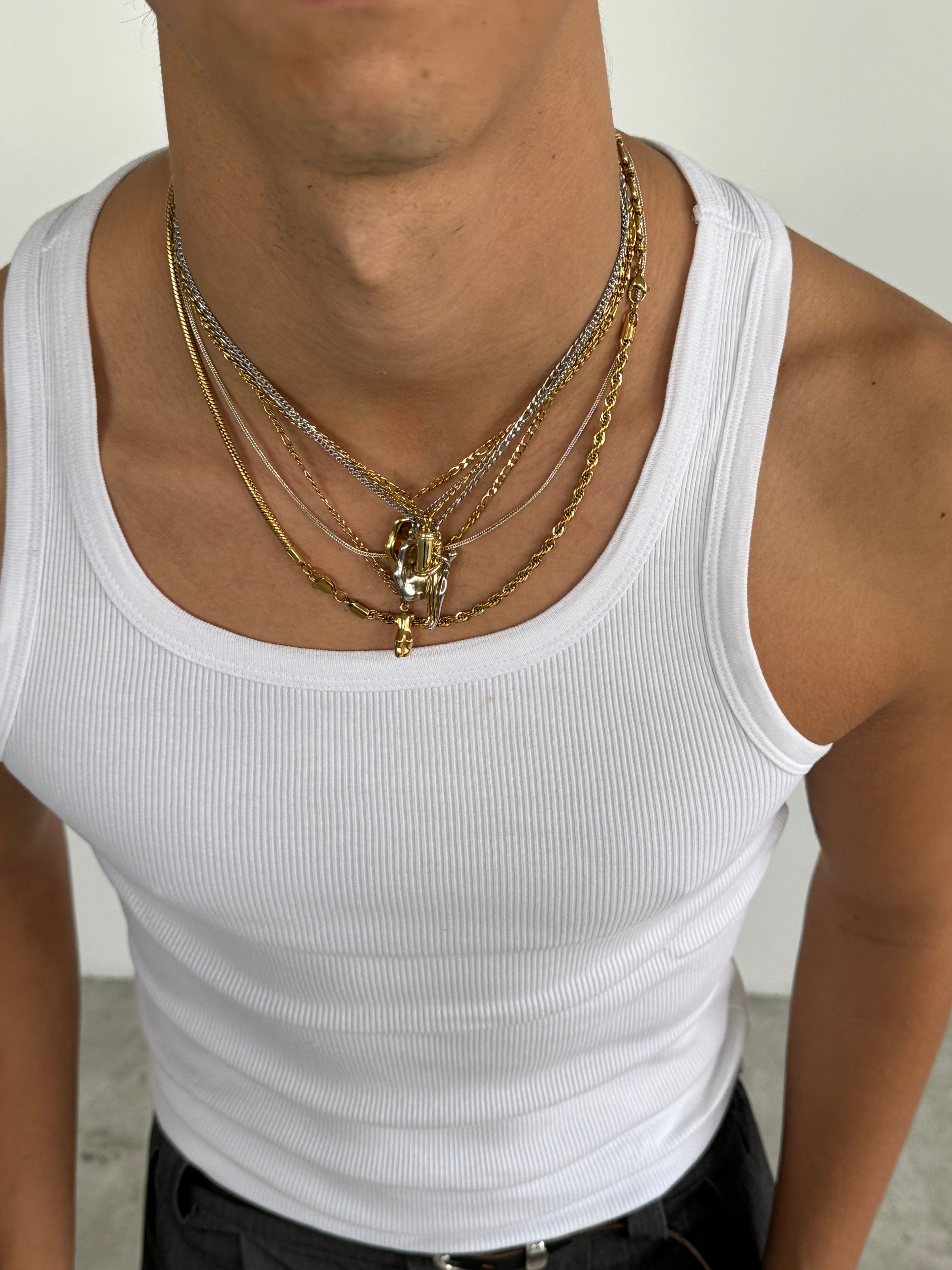 Person wearing a white tank top with layered gold and silver necklaces.