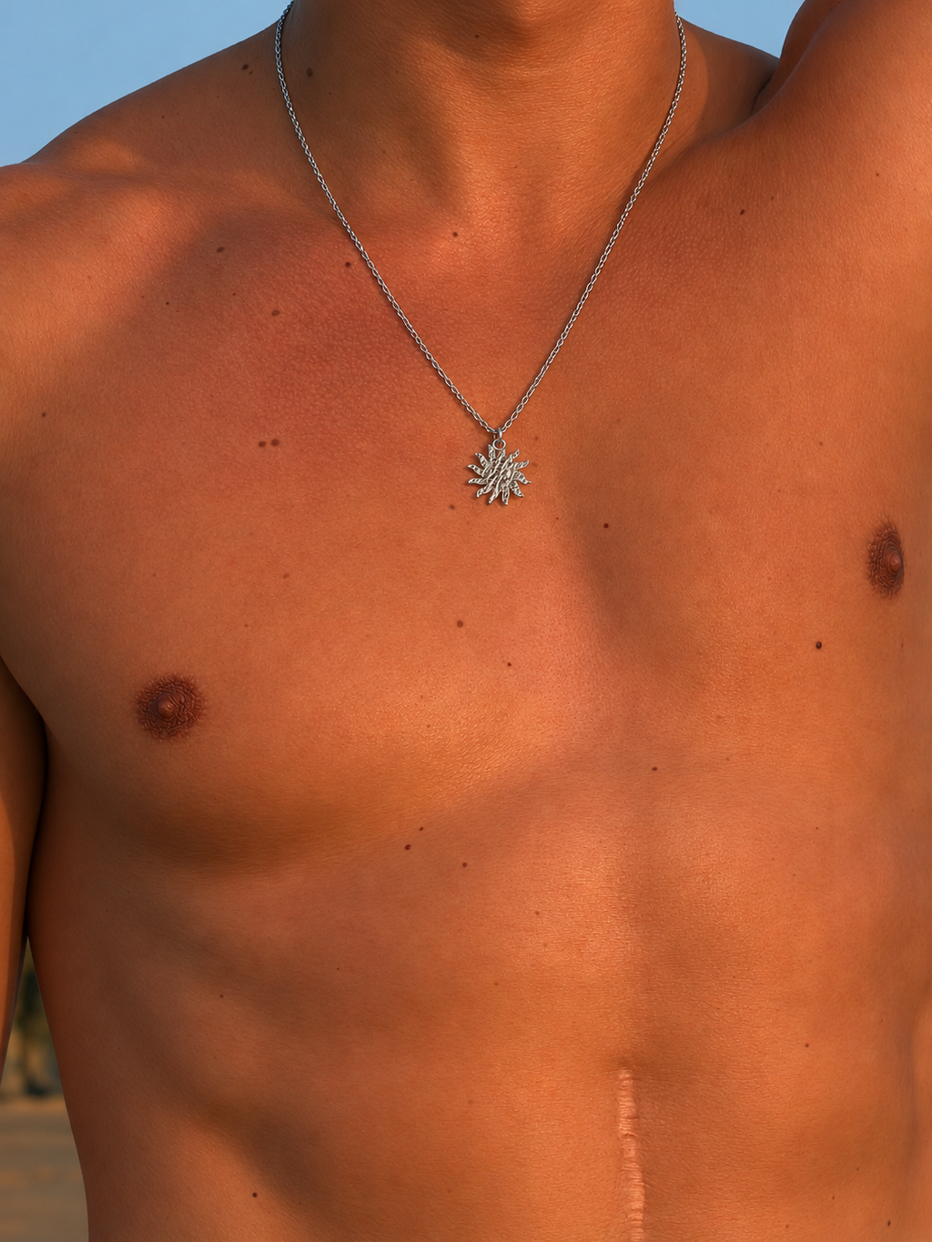 Man wearing a silver necklace with a sun pendant on a blurred background