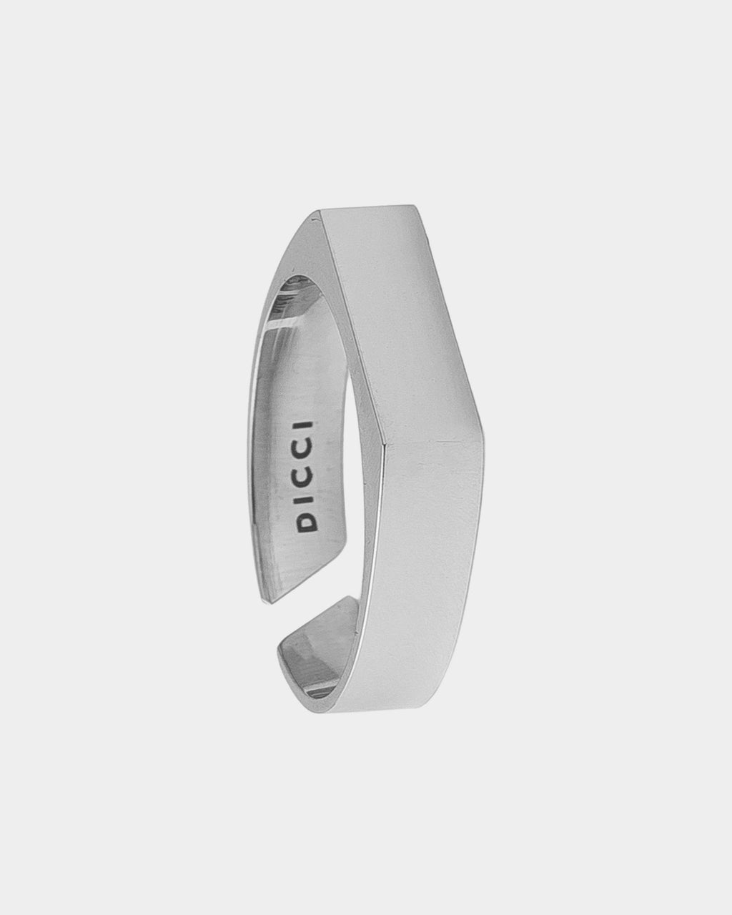 Un anillo brazalete abierto de tono plateado con acabado mate y el nombre de la marca «DICCI» grabado en el interior, sobre un fondo gris claro.