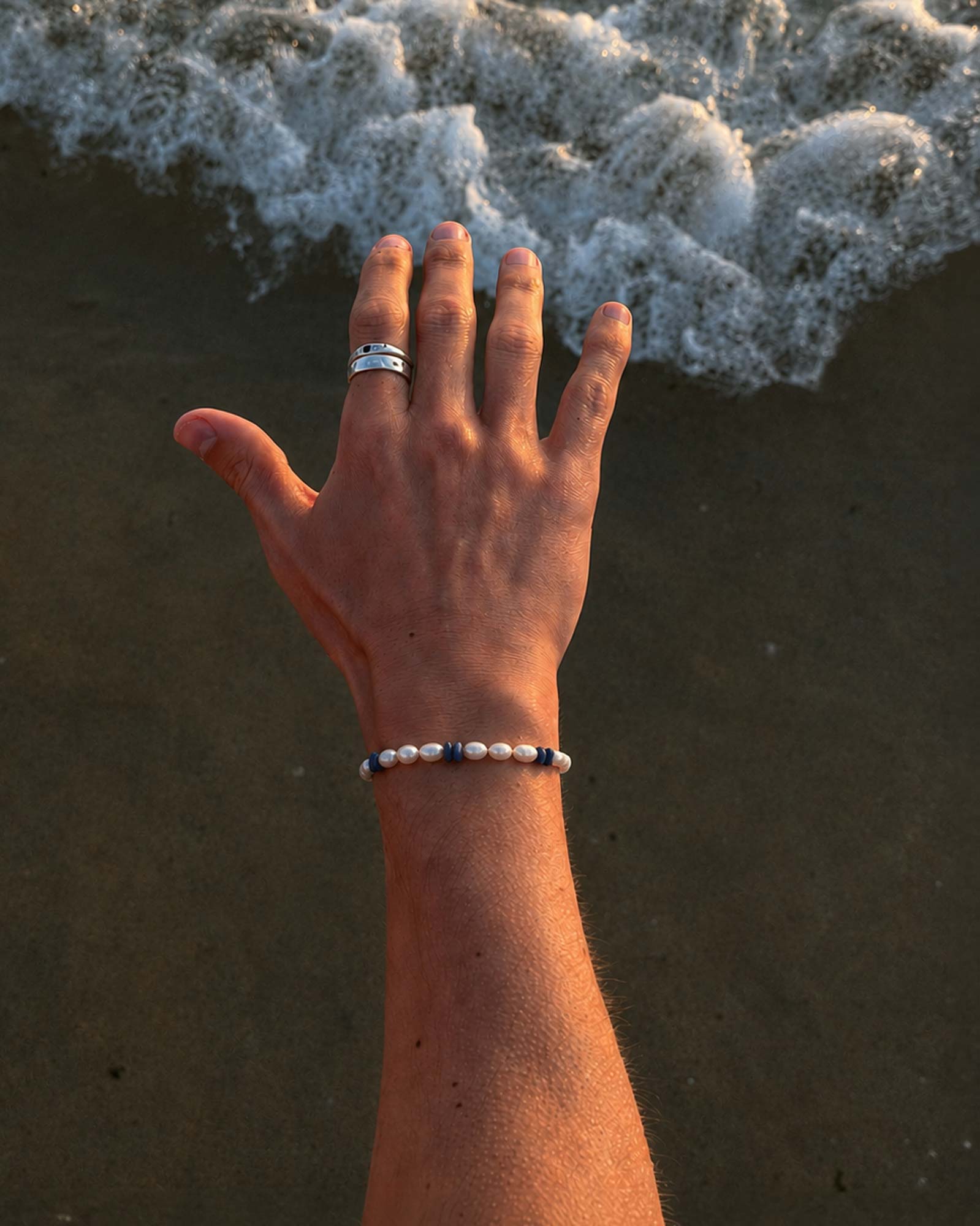 Hand with a bracelet and ring on a beach with waves in the background