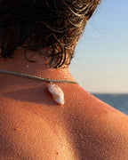 Person wearing a necklace with a shell pendant by the ocean