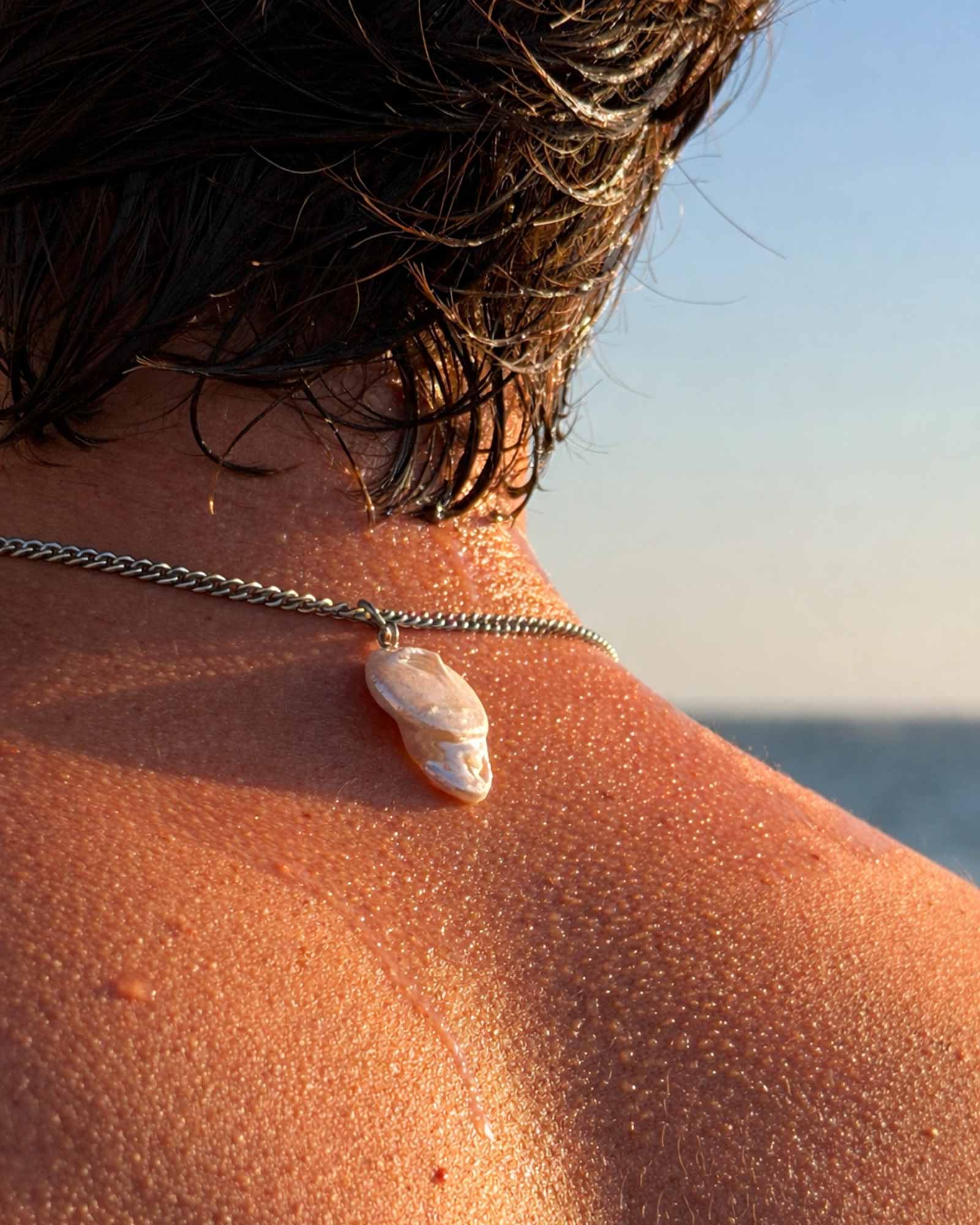 Person wearing a necklace with a shell pendant by the ocean