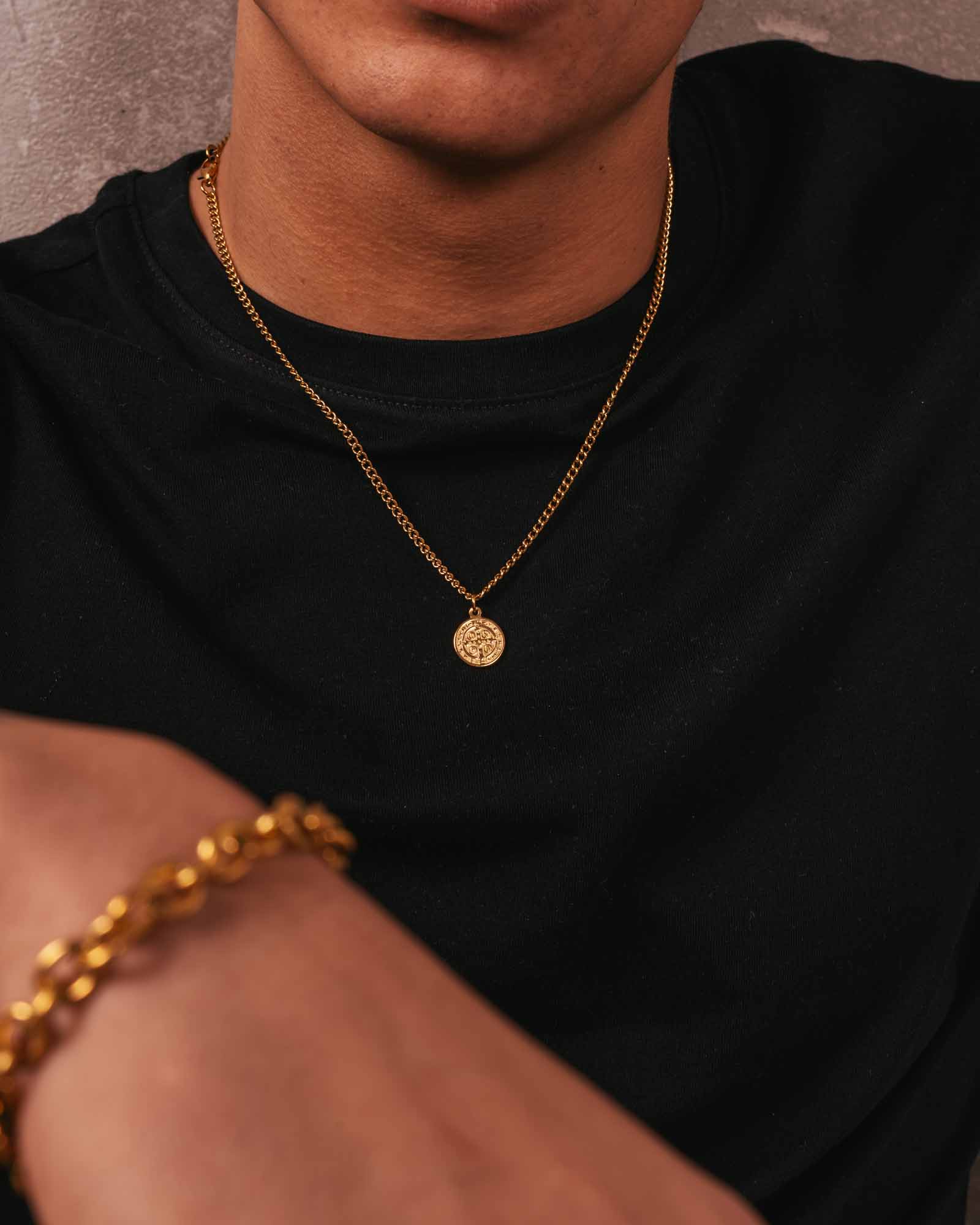 Person wearing a golden St. Benedict's necklace with a white shirt