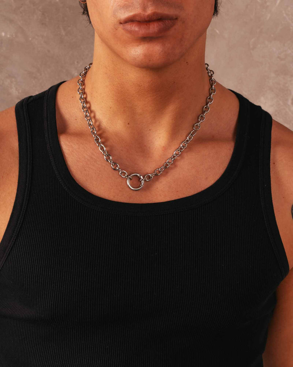 Person wearing a black tank top and a chain necklace against a neutral background