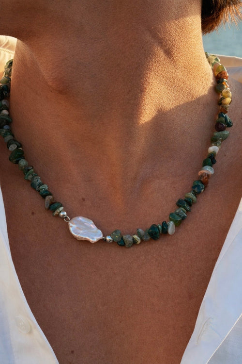 Necklace with green stones and a white clasp on a person wearing a white top.