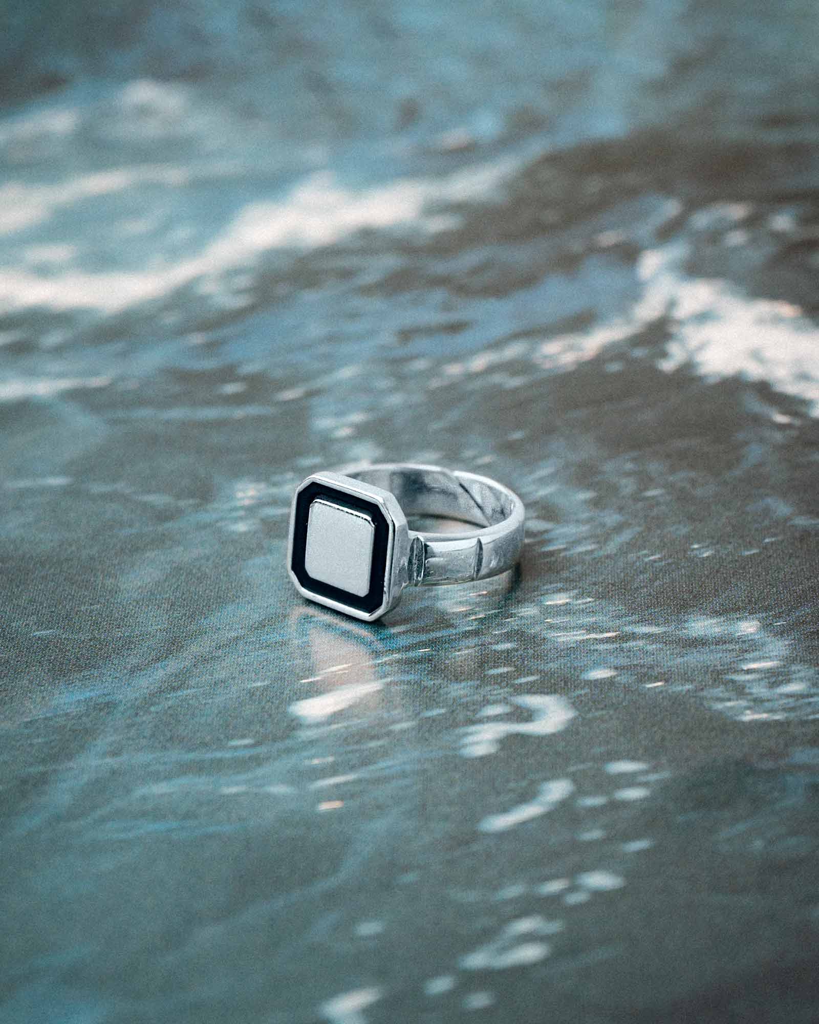 Silver ring with a square black center on a sandy surface