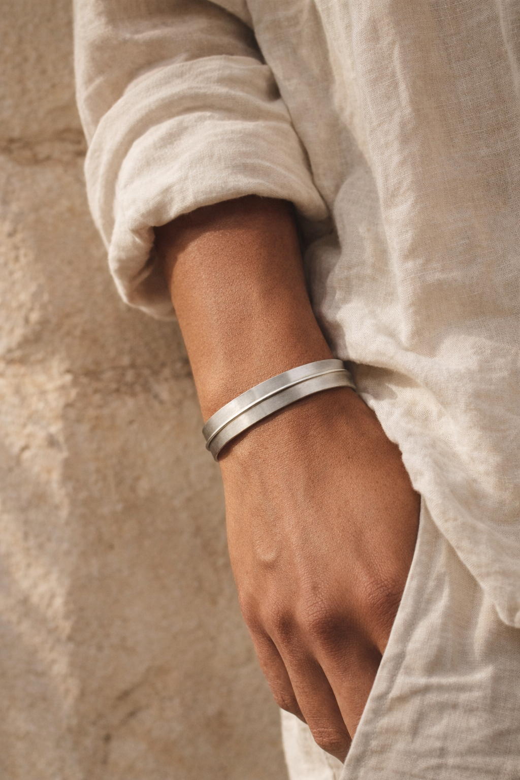 Close-up of a person wearing two silver bracelets on a neutral background