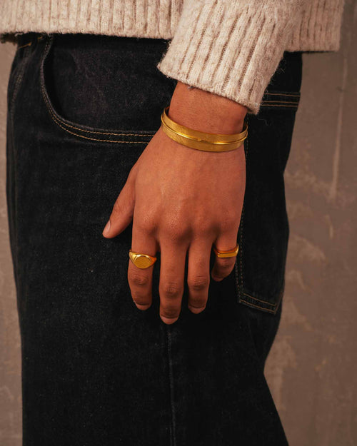 Hand wearing gold bracelets and rings on a neutral background
