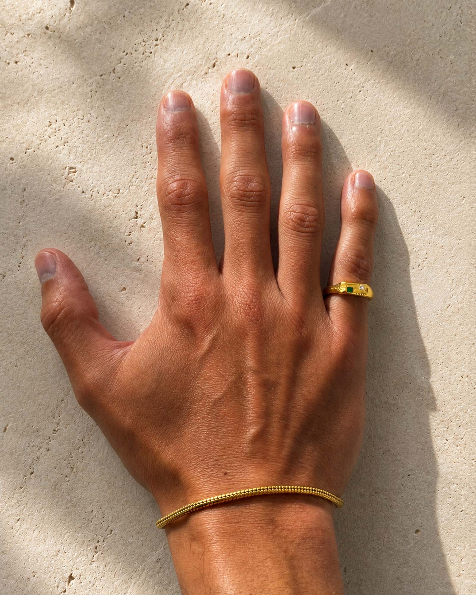 Hand with a gold ring and bracelet on a beige background